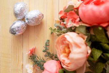 White eggs and eggs in foil on the wooden background with flowers and cotton around. Eggs in the basket