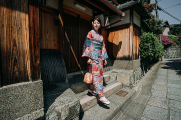 Fototapeta na wymiar local female teenager girl going out from home walking down stairs to join summer festival wearing colorful kimono under sunshine. elegant japanese woman in traditional dress live old wooden house