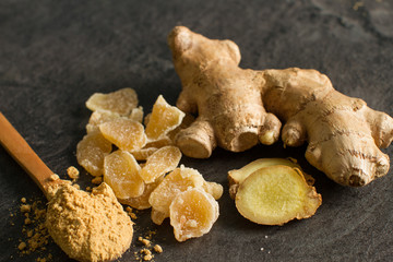 Ginger root, candied and ginger powder in wooden spoon over grey concrete background