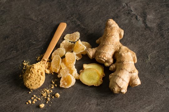 Ginger root, candied and ginger powder in wooden spoon over grey concrete background