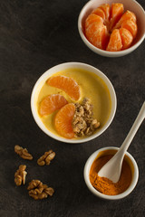 Tasty tangerine smoothie bowl with fruits, cereals, seeds and turmeric powder over  grey background