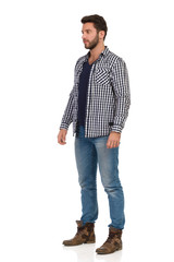 Young Man In Boots, Jeans And Lumberjack Shirt Is Standing And Looking Away