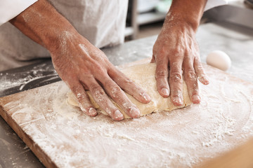 Fototapeta premium Closeup portrait of beautiful male hands making dough for bread, on table at bakery or kitchen