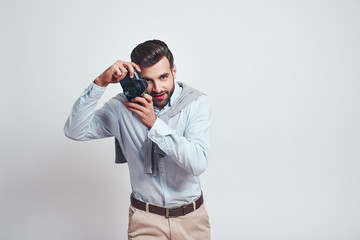 Nice shot. Attractive young man in casual wear is photographing you while standing in studio on a grey background
