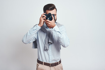 Do what you love. Young bearded man in blue shirt taking picture with camera isolated on grey background.
