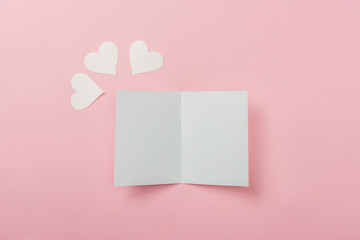 white blank greeting card and paper hearts on pink background