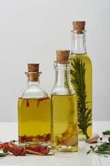 bottles of oil flavored with rosemary and various spices on white surface