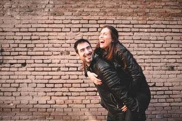 Fototapeta na wymiar Girl riding on the back of her boyfriend laughing and having fun together as they look young and happy.