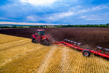 red tractor cultivates the land for planting crops. Aerial view of cultivated land tractor