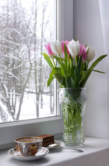vase with white and pink tulips on the windowsill, a Cup of tea, chocolate cake near the window
