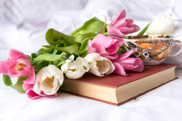 few white and pink tulips, a book, a tea mug, a white sheet