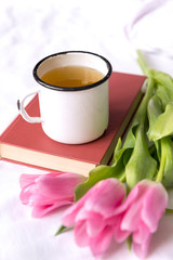 Obraz na płótnie Canvas white metal tea mug on the book, pink tulips