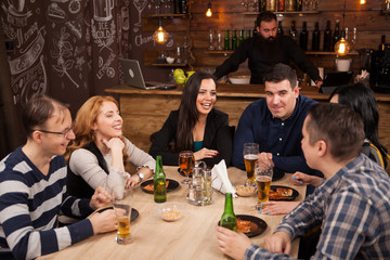 Group of young friends sitting around table in bar togethe