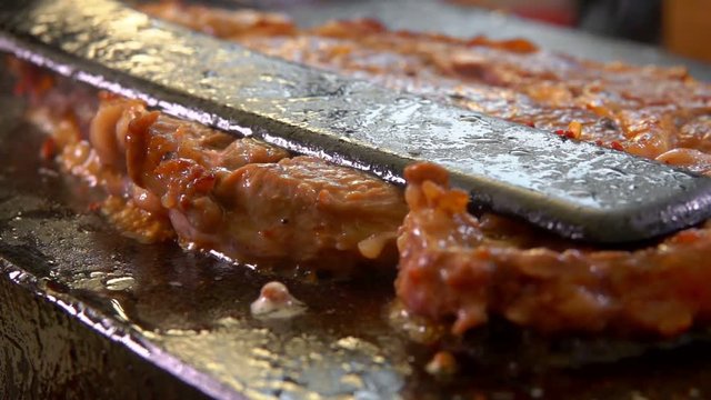 Cook presses the steak on the hot surface of the stone grill with a spatula