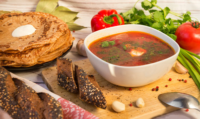 soup, a plate of borscht with greens and sour cream, bread, pancakes, vegetables