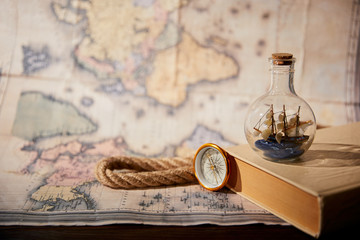 Fototapeta na wymiar Selective focus of toy ship in glass bottle, book, map, compass and rope