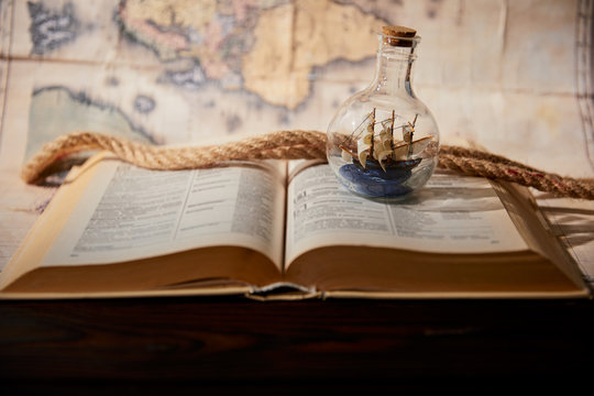 Selective focus of toy ship in glass bottle, book, map and rope on table
