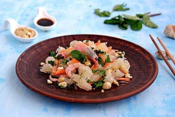 Refreshing salad with pomelo, shrimps, carrots and cashew nuts on a light blue background. Asian cuisine.