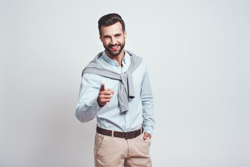 Fototapeta premium I choose you! Happy and smiling handsome man pointing his finger and looking positive at camera while standing against grey background