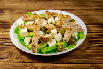 Tasty salad with fried chicken breast, green olives, feta cheese, avocado, lettuce and olive oil on wooden table