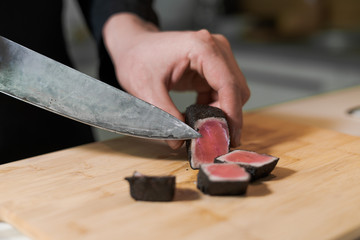 cook cut with knife slices of medium rare grilled tuna meat on wooden platter