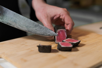 cook cut with knife slices of medium rare grilled tuna meat on wooden platter