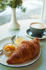 Delicious fresh breakfast. Fresh croissant with jam and butter and a cup of coffee on grey table.