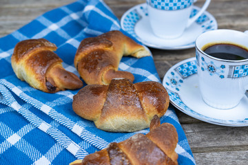 Two cups of coffee, homemade croissants with chocolate on a blue cloth and wooden boards.
