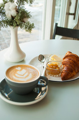 Delicious fresh breakfast. Fresh croissant with jam and butter and a cup of cappuccino with beautiful latter art.