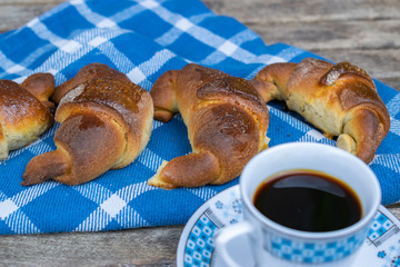 Homemade croissants, a cup of coffee on a blue cloth and wooden background.