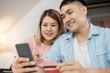 boyfriend hand holding mobile and credit card to shopping online for girlfriend on kitchen table in home.couple lifestyle concept.