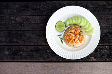 Shrimps fried rice serve with fresh cucumber and fresh lime and green chilli in round plate on vintage old wood background, healthy food concept
