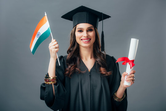 happy student in academic gown and graduation cap holding diploma and indian flag, isolated on grey - Powered by Adobe