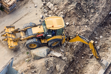 Yellow tractor with a bucket and back and front, digging a trench at a construction site. View from above.
