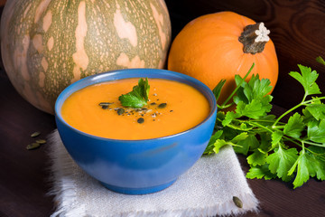 Pumpkin vegetarian soup in a blue bowl served with parsley, olive oil and pumpkin seeds on a dark wooden background.