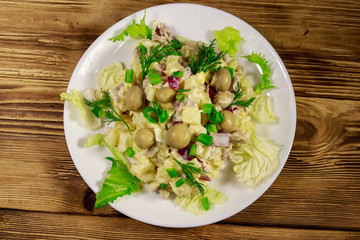 Potato salad with marinated mushrooms, eggs, red onion and mayonnaise on wooden table