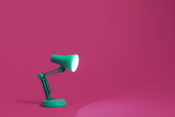 Vintage green desk lamp on a bright pink background.  Lamp turned on and shining out to the edge of...