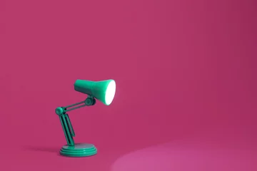 Foto op Aluminium Vintage green desk lamp on a bright pink background.  Lamp turned on and shining out to the edge of the image.  Copy space and room for text. © George