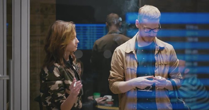 Young beautiful couple travelers smoke at the bus station