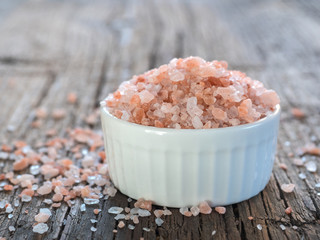 Fototapeta na wymiar Pink Himalayan salt in white salt shaker on wooden background. Healthy spice closeup