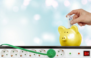 saving electricity costs, hand puts money into piggy bank.