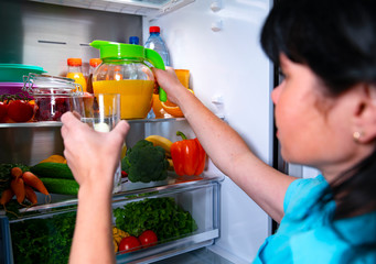 Open fridge. A woman holds a glass in her hand and pours fresh juice from a jug. Fresh vegetables and fruits.