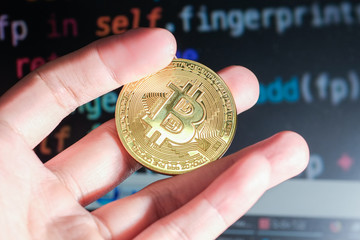 A hand holding a gold coin with a lot of lines of programming code as a background. Cryptocurrency...