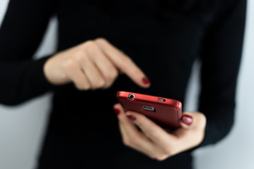 Closeup detail of young woman holding a red cell phone with camera using a touchscreen with apps to connect on social media, texting, chatting and messaging