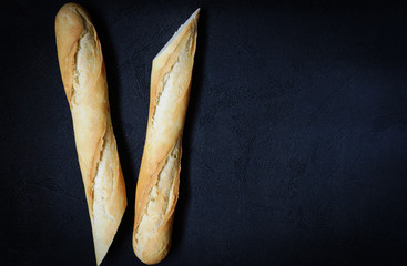 Fresh french roll baked crunchy baguette bread on dark background. Closeup of crust of bread food background. Top view. Natural lighting