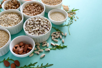 Set of bowls with organic quinoa, lentil, chickpea, wheat, walnut, almond, hazelnut and sesame. Cereals and legumes assortment on blue paper background. Top view. Copy space. Flat lay