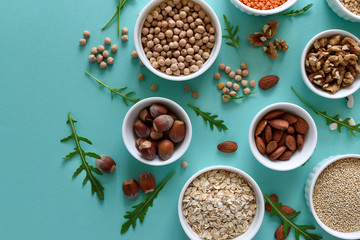 Set of bowls with organic quinoa, lentil, chickpea, wheat, walnut, almond, hazelnut and sesame. Cereals and legumes assortment on blue paper background. Top view. Copy space. Flat lay