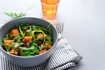 Salad with arugula,pumpkin and pomegranate seeds on gray wooden background. Vegetarian food concept. Selective focus.