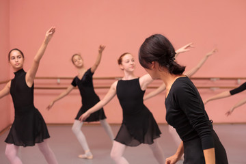 Obraz premium Mid adult female ballet teacher instructing medium group of teenage girls in black dresses