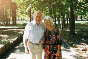 Beautiful old couple are walking in the park. Grandma and grandpa are hugging outdoors. Happy golden wedding anniversary. Romantic photo of grandmother and grandfather. Real love.